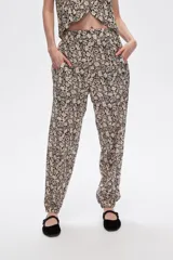 Pantalón slouchy de viscosa con estampado floral en tonos beige y negro, bolsillos laterales, cintura alta y detalle de punto smock en los tobillos.