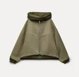 Campera corta color verde oliva, de corte holgado, con cuello alto acolchado y cierre frontal con cremallera. Posee mangas largas con puños elásticos.