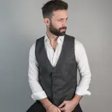 Chaleco de vestir marrón claro con textura de espiga, cuello en V, cierre frontal con botones y bolsillos ribeteados.