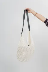 Bolso tejido color crudo con textura calada y correa de eco-cuero negra regulable con hebilla metálica.