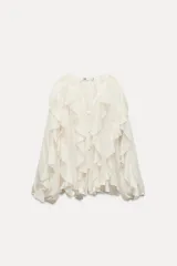 Blusa color crudo de escote pico y manga larga abullonada con volantes en el mismo tejido y cierre frontal con botones.