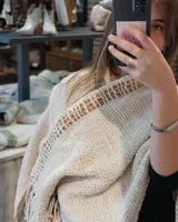 Ruana color crema tejida a mano con detalles de cuero en los bordes y flecos.