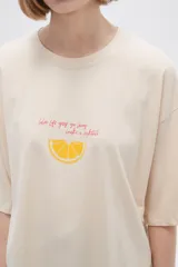 Remera color crema con estampado de limón y texto en color naranja.
