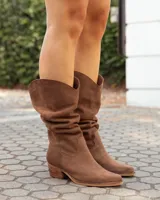 Botas texanas de caña media confeccionadas en cuero gamuzado color marrón. Presentan un diseño de corte clásico con costuras decorativas en el empeine, puntera levemente redondeada y taco bajo de madera.