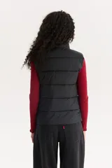 Chaleco acolchado negro con cuello alto y cierre frontal con cremallera. Tiene un logo pequeño de la marca en el pecho.