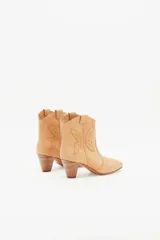 Botín de cuero color beige, estilo cowboy, con bordados en forma de mariposa en los laterales y taco de madera.