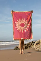 Pareo rectangular fucsia con estampado de sol dorado y borde con diseño geométrico en tonos naranja y marrón.