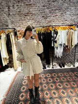 Mono color beige confeccionado en lino, con mangas globo, cierre frontal, cuello elegante, bolsillos y cinto para ajustar en la cintura.