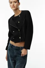 Blazer negro de cuello redondo y manga larga, con costuras a contraste y cierre frontal con botones metálicos dorados. Forro interior a tono.