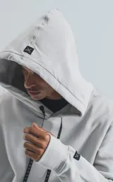 Hoodie gris claro, de corte oversize, confeccionado en frisa premium. Posee capucha ajustable, bolsillo canguro frontal y puños y cintura elastizados. Los cordones de la capucha son negros con texto repetido.