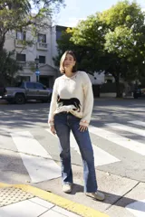 Sweater tejido color crema con cuello y puños acanalados en color naranja. Presenta un diseño bordado de un perro salchicha negro con un moño naranja.