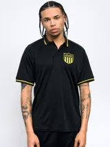 Remera polo negra de poliéster con cuello clásico y mangas cortas. Presenta ribete amarillo en cuello y mangas, escudo del Club Atlético Peñarol bordado en el pecho y corte regular.