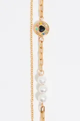 Pulsera dorada de doble cadena, una de eslabones y otra con perlas. Incluye un dije redondo con un corazón negro y logo grabado.