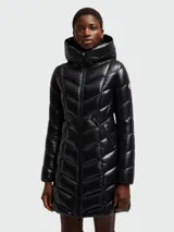 Campera larga de pluma Moncler modelo Marus, color negro con acabado brillante. Presenta un diseño acolchado con costuras en zigzag, capucha integrada, cierre frontal de cremallera y bolsillos laterales con cierre. Incluye el parche con el logo de la marca en la manga.