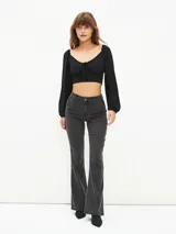 Blusa crop top negra con escote cuadrado, mangas largas abullonadas y lazo ajustable en el centro del busto.