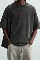 Camiseta negra con efecto lavado, corte boxy fit, cuello redondo y manga corta. Estampado rojo en el frente.