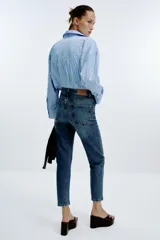 Pantalón de jean azul de tiro alto, corte mom fit, tobillero y con cinco bolsillos. Cierre frontal con cremallera y botón.