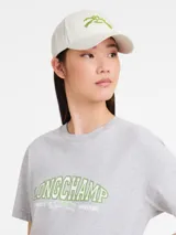 Gorra de béisbol color crema con logo bordado en verde en el frente.