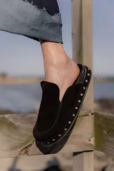 Zuecos de gamuza color marrón chocolate, con base de goma negra, tachas plateadas alrededor de la base y plantilla acolchada.