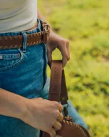 Bandolera de cuero color marrón con correa larga regulable, solapa con diseño trenzado y cierre con broche imantado.