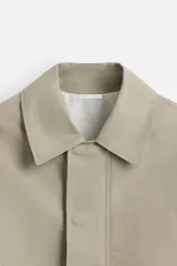 Cazadora color arena confeccionada en tejido con mezcla de algodón y lino. Tiene cuello solapa, manga larga, bolsillos de doble vivo en la cadera y bolsillo interior. Los acabados son con elástico. El cierre frontal es con cremallera oculta por solapa con botones a presión.