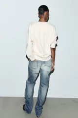 Sudadera de tejido mezcla de algodón color crema, con cuello redondo y manga larga. Presenta un estampado central con el texto "SOHO NOHO" en tipografía alargada, con las letras alternando entre azul y verde.