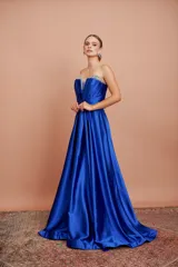 Vestido largo de fiesta color azul eléctrico, strapless, con escote corazón y detalle de piedras brillantes en el borde superior. Tiene corte imperio con falda amplia y plisada.