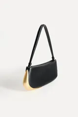 Bolso de hombro alargado color crema, con asa corta y detalle metálico dorado en un lateral. Tiene un bolsillo interior con cremallera y cierre principal con cremallera.