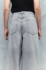 Pantalón jean gris claro, de corte holgado con pierna ancha y tiro bajo. Diseño clásico de cinco bolsillos con cierre frontal con cremallera y botón.