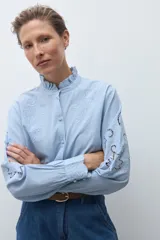 Camisa de algodón celeste claro, de manga larga, con cuello mao con volados y bordados calados florales en el frente y las mangas.
