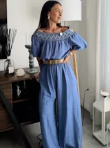 Enterito largo color azul, con escote Bardot y bordado blanco en el borde superior. Presenta mangas cortas abullonadas y pantalón ancho. Se ajusta a la cintura con un lazo de tela del mismo material.