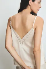 Conjunto de pijama color crema con detalles de encaje en el top. El top es de tirantes finos y el pantalón es largo con volados en el ruedo.