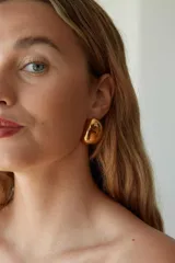 Aros tipo caravanas doradas con forma irregular, confeccionadas en acero quirúrgico hipoalergénico.