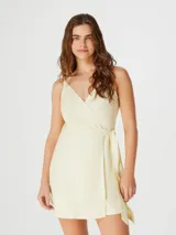 Vestido corto color amarillo pálido, con breteles finos, escote en V cruzado y lazo en la cintura.