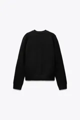 Chaqueta de punto negra con cuello redondo y manga larga. Presenta detalle de lazos con abalorios en el frente y cierre con botones a presión.