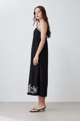 Maxi vestido negro de breteles finos con escote recto y bordado floral en el ruedo.