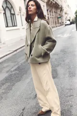 Abrigo corto color verde oliva, de cuello solapa y manga larga. Cuenta con bolsillos delanteros de vivo y cierre frontal cruzado con botones.