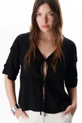 Chaqueta ligera de lino color negro con cierre frontal mediante lazos. Presenta escote en V, mangas de largo medio con detalles de volados fruncidos y un diseño fluido de inspiración romántica.