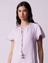 Vestido corto de lino a rayas verticales color lila y blanco, con cuello fruncido, escote en V y lazo de ajuste. Mangas cortas con puntilla de crochet.