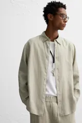 Camisa color arena de lino con cuello abotonado, manga larga con puños abotonados, corte regular y bajo con aberturas laterales.