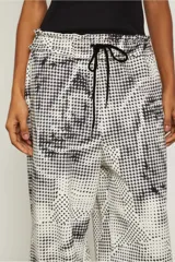Pantalón amplio con estampado abstracto en blanco y negro, cintura elástica ajustable con cordón y tobillos fruncidos.
