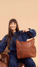 Cartera tipo hobo de cuero sintético color marrón con correa corta y correa larga ajustable. Tiene un bolsillo con cierre en el frente y otro en la parte trasera, además de bolsillos internos.