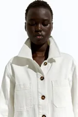 Campera color crudo en sarga de algodón con cuello, botones adelante y canesú en la espalda. Modelo de hombros apenas caídos con bolsillos superiores de parche, bolsillos insertados adelante y puños abotonados.