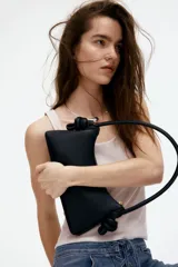 Bolso de hombro pequeño color negro, con cierre superior y asa rígida con nudos decorativos en los extremos. Forro de tafeta.