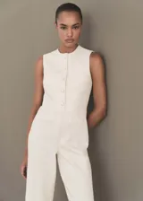 Mono largo color crudo confeccionado en tejido tweed, con cuello redondo, sin mangas y cierre frontal con botones. Presenta dos bolsillos de ribete delanteros y diseño recto.