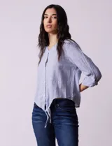 Blusa de algodón a rayas verticales azules y blancas, con cuello en V, mangas 3/4 y cierre frontal con botones. Tiene un nudo en la parte delantera.