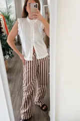 Blusa blanca sin mangas con cuello mao, volados en cuello, sisas y ruedo, y cierre frontal con botones.