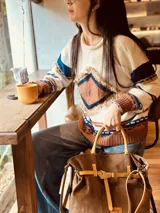 Bolso marrón de cuero gamuza con detalles de correa en cuero mostaza. Tiene una correa corta para llevar como bolso de mano y una correa larga extraíble y regulable. En el interior tiene bolsillo y llavero.