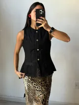 Chaleco negro de denim con corte peplum, cuello redondo y cierre frontal con botones dorados.