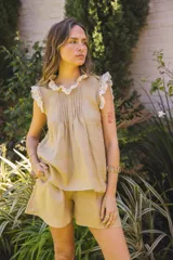 Blusa color beige de lino natural, sin mangas, con cuello fruncido y volados de encaje en las mangas. Presenta pinzas frontales.